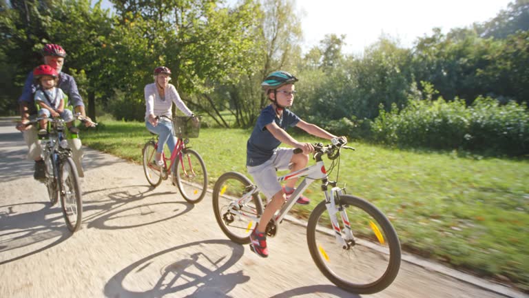 TS Grandparents riding bikes in sunny park with one grandson riding his bike in front and other in the seat