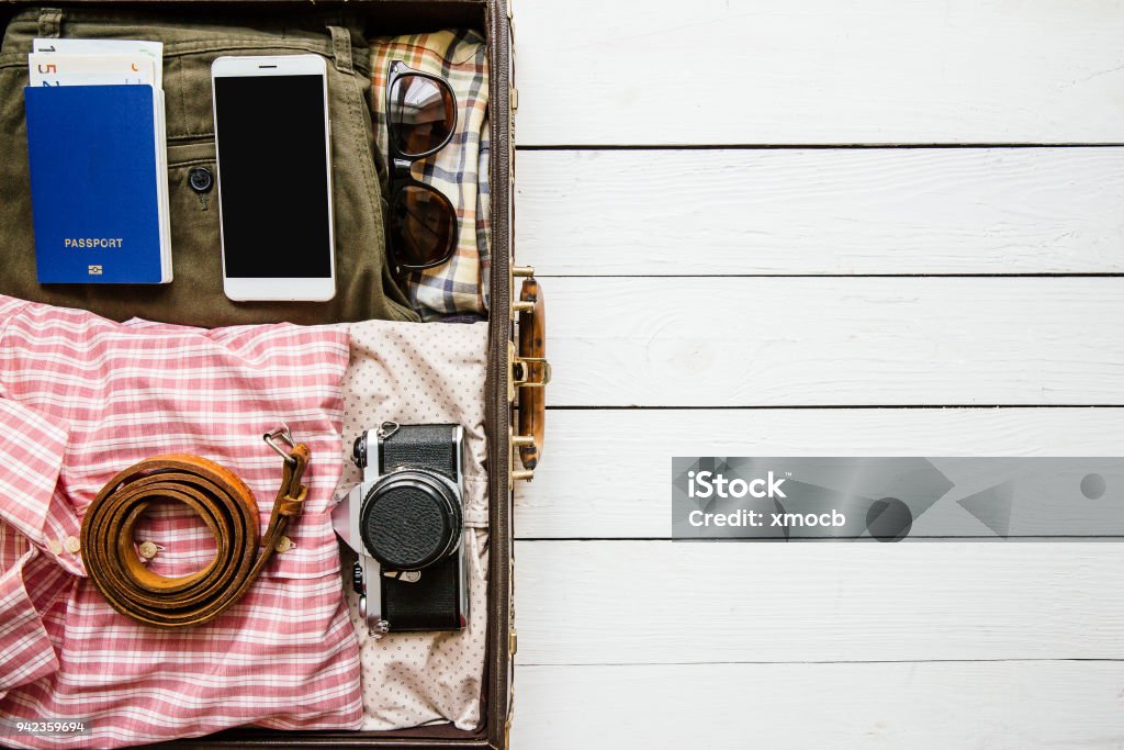 Packing suitcase travel concept Vintage hipster clothes, shoes, hat, smartphone, accessories packed in suitcase on white wooden table. Travel concept. Empty space for copy, text, lettering. Suitcase Stock Photo