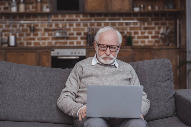 istock handsome grey hair man sitting on sofa in living room and using laptop 942393686