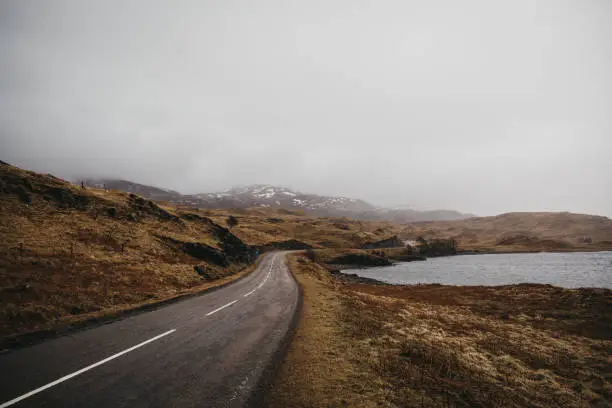 Road going through Scottish Highlands near Lochinver on a foggy spring day.