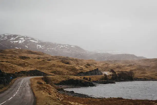 Road going through Scottish Highlands near Lochinver on a foggy spring day.