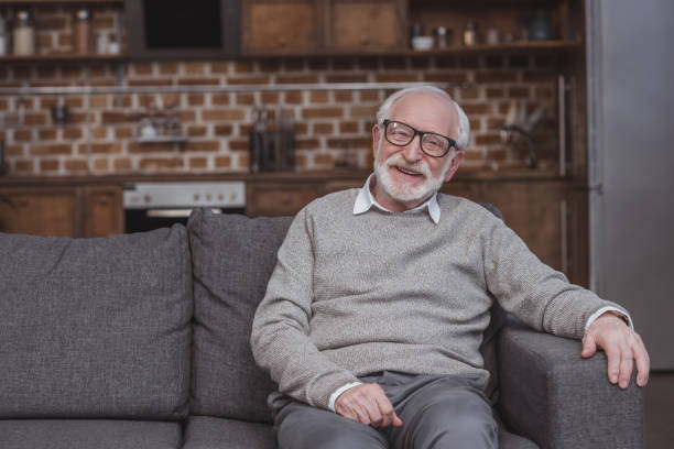 istock smiling handsome grey hair man sitting on sofa at home 942396766