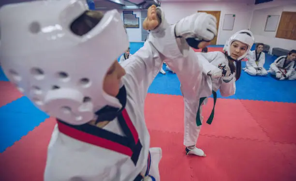 Group of people, taekwondo kids team training indoors, two children fighting.