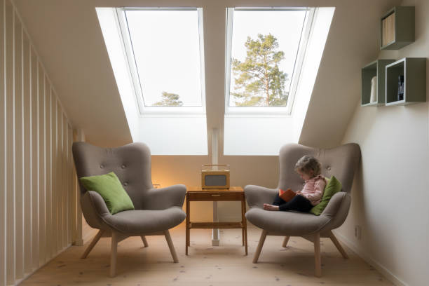 Small child reading a book under a skylight Modern retro design in a attic / loft. Small vintage table with a radio on and two reading chairs under two skylights with a little child reading a book. skylight stock pictures, royalty-free photos & images