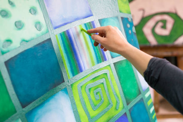 Detail of artists hand holding pastel crayon and painting in her studio.