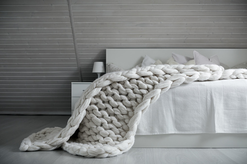 Cozy white scandinavian bedroom interior. Beautiful merino woolen plaid decorated bed and floor, super chunky yarn knitted blanket, nobody