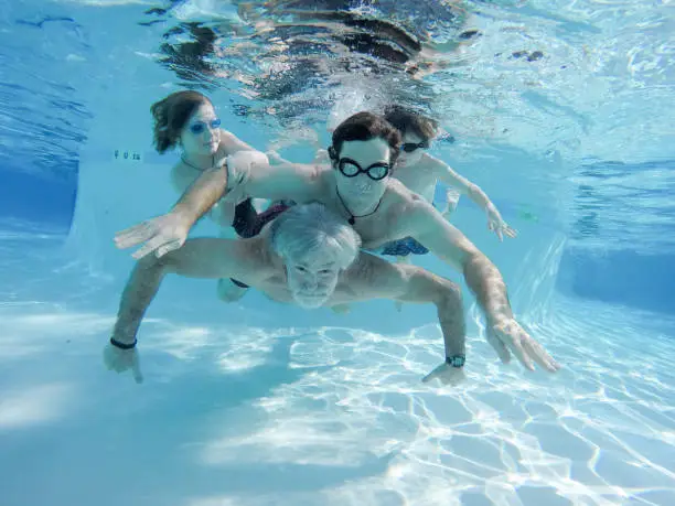 Father and Grandfather swim in children underwater on beautiful sunny summer day