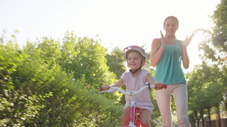 SLO MO Mom letting go of the bike her young daughter is riding for the first time on a sunny street