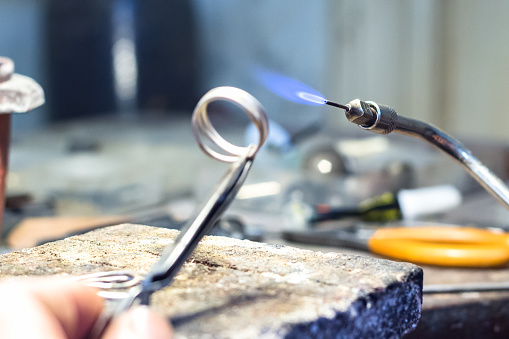 Jeweler welding a silver piece with a mini gas - oxygen torch welder.