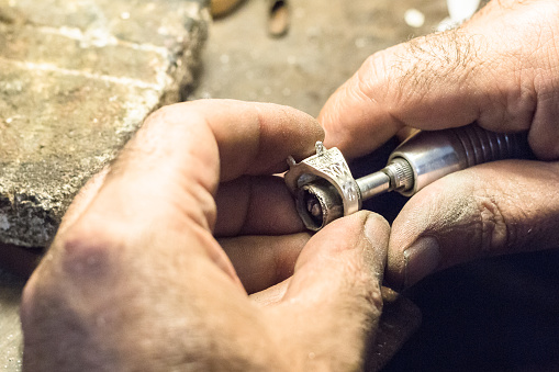 Male jeweler polishing a silver ring with a slotted mandrel for sandpaper, mounted on a flex shaft.