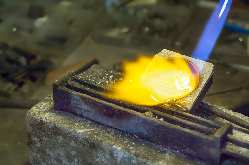 Jeweler putting melting silver on wire ingot mold using a gas - oxygen torch.