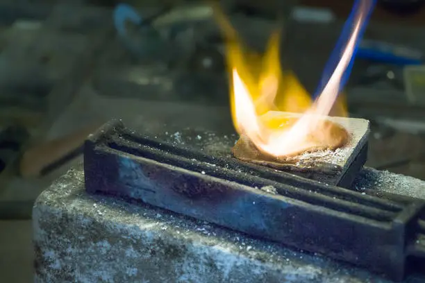 Jeweler melting silver on a ceramic melting pot with a gas torch and a wire ingot mold ready to use.