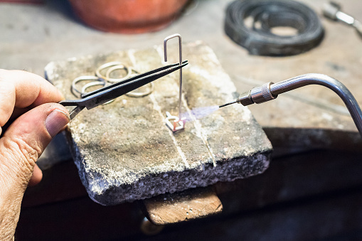 Jeweler holding a piece with a tweezers while welding with a mini gas - oxygen welding torch.