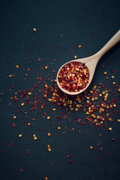 istock Red Chilli flakes in wooden spoon on dark black background,top view copy space 942459472