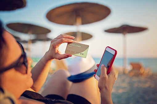 Woman is shopping online using her credit card on the beach