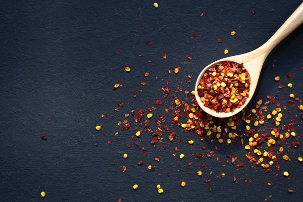 istock Red Chilli flakes in wooden spoon on dark black background,top view copy space 942459992