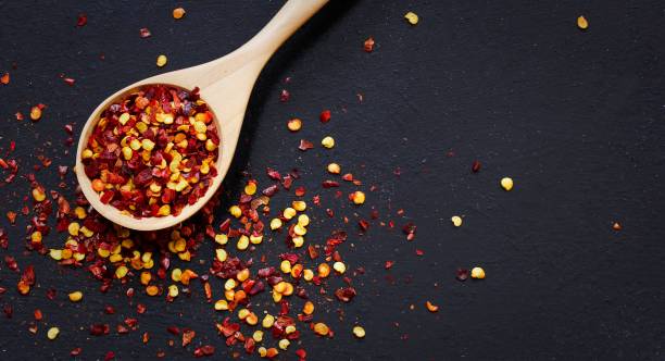 istock Red Chilli flakes in wooden spoon on dark black background,top view copy space 942460196