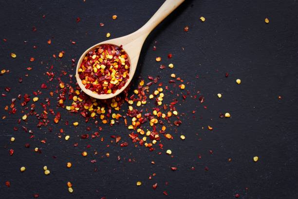 Red Chilli flakes in wooden spoon on dark black background,top view copy space