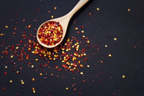 Red Chilli flakes in wooden spoon on dark black background,top view copy space Red Chilli flakes in wooden spoon on dark black background,top view food styling stock pictures, royalty-free photos & images