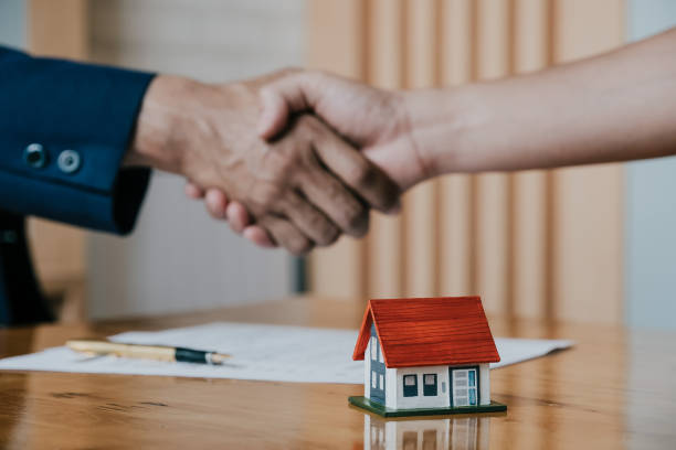 istock Estate agent shaking hands with his customer after contract signature, Contract document and house model on wooden desk 942466966