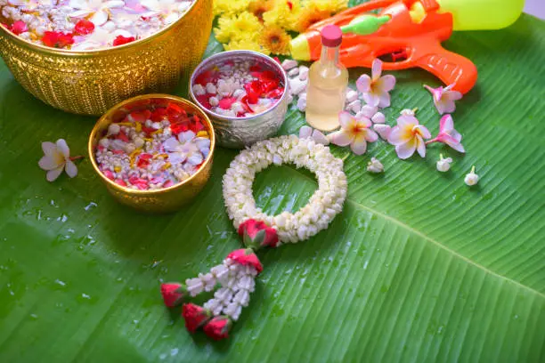 Photo of Thai traditional jasmine garland and Colorful flower in water bowls decorating and scented water, perfume, marly limestone, pipe gun on Banana leaf for Songkran Festival or Thai New Year