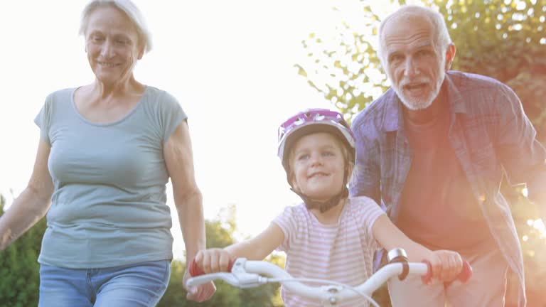 SLO MO Grandparents helping granddaughter ride the bike for the first time and cheering for her