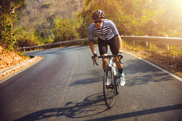 los hombres asiáticos son ciclismo bicicleta de carretera en la mañana. él está en un camino forestal. - casco de deportes fotos fotografías e imágenes de stock