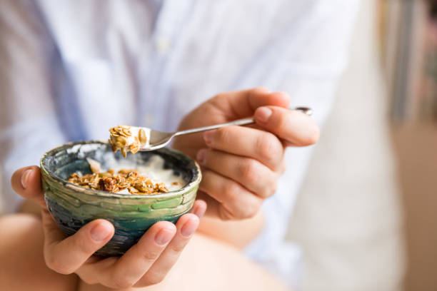 jeune femme avec bol de muesli. fille, manger des céréales de petit déjeuner avec les noix, les graines de citrouille, avoine et l’yogourt dans un bol. granola maison de fille tenue. collation ou petit déjeuner le matin. - cereal breakfast granola healthy eating photos et images de collection