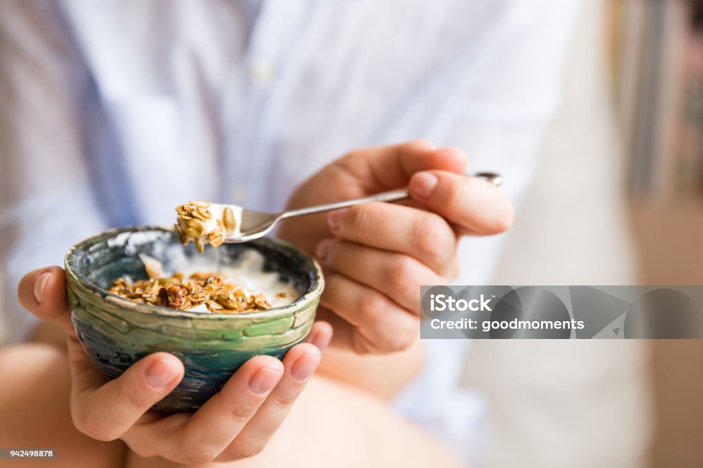 Giovane donna con ciotola muesli. Ragazza che mangia cereali per la colazione con noci, semi di zucca, avena e yogurt in ciotola. Ragazza che tiene in mano muesli fatti in casa. Spuntino sano o colazione al mattino. - Foto stock royalty-free di Yogurt