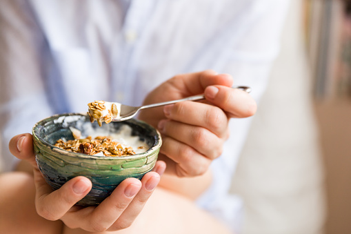 Young woman with muesli bowl. Girl eating breakfast cereals with nuts, pumpkin seeds, oats and yogurt in bowl. Girl holding homemade granola. Healthy snack or breakfst in the morning..