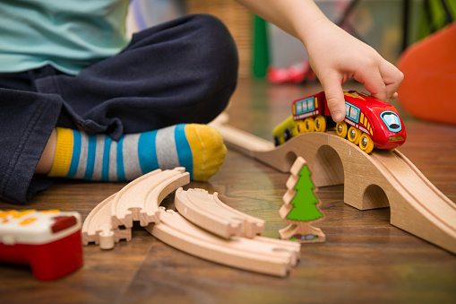 Close up on child's hands with toy train and railway in his room. Boy playing indoors.