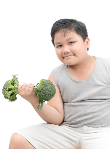 istock Overweight boy holding a broccoli dumbbell isolated 942514334
