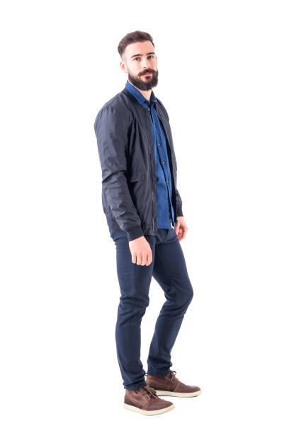 Side view of confident relaxed macho guy in bomber jacket posing and looking at camera