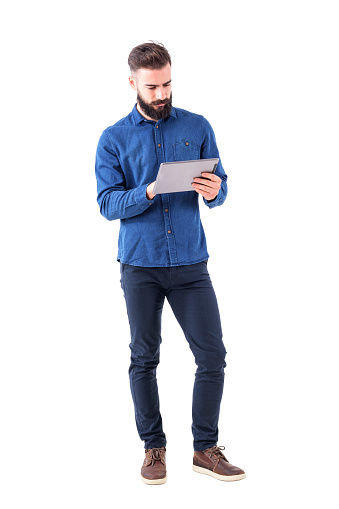 Confident serious bearded business man using tablet touch pad screen. Full body isolated on white background.