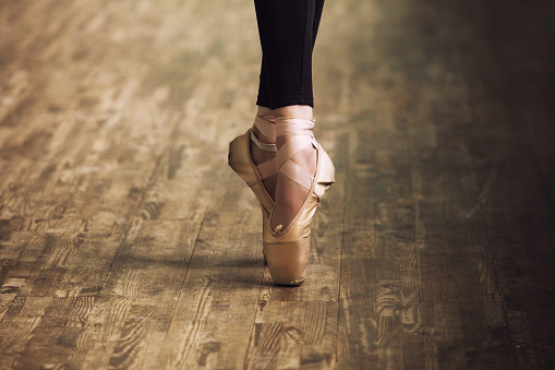 Feet of ballerina in training shoes on the parquet wooden floor close up retro style