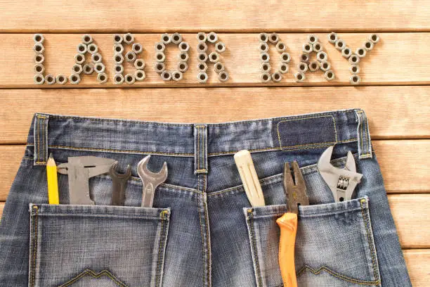 Labor day.  Various tools in blue jeans on wooden table