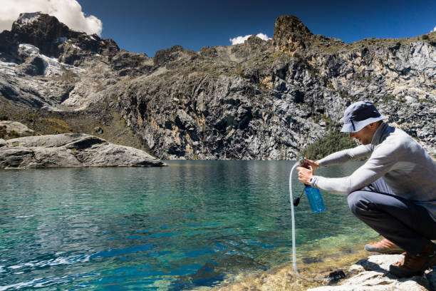 male mountain climber filtering drinking water from a turquoise mountain lake male backpacker dressed in gray filters drinking water from a turquoise mountain lake in the Cordillera Blanca in the Andes in Peru giardia lamblia stock pictures, royalty-free photos & images