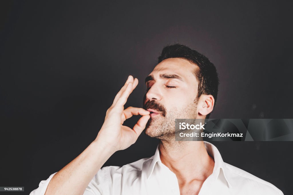 Young handsome man with beard and mustache studio portrait Young handsome man with beard and mustache kissing fingers, hand gesture for perfection Italian Ethnicity Stock Photo