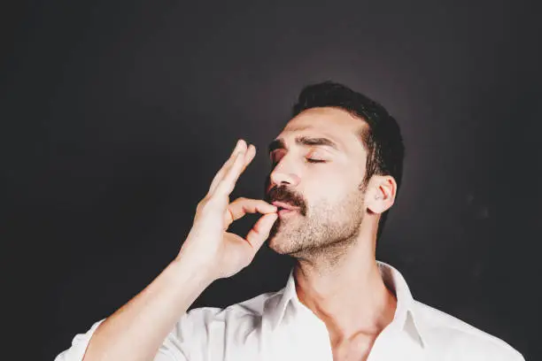 Young handsome man with beard and mustache kissing fingers, hand gesture for perfection