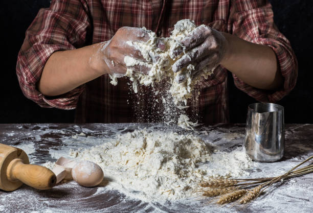 istock Man preparing bread dough on wooden table in a bakery close up 942547712