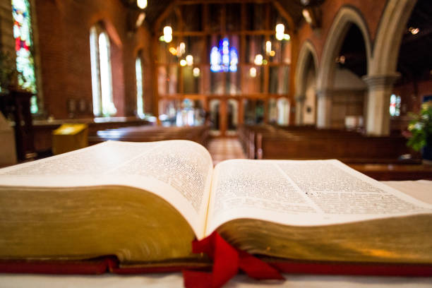Close up of open bible on altar of Anglican church Color image depicting a close up wide angle view of the pages of an open bible on the altar of an Anglican church. Focus is on the bible in the foreground, while the background consists of the defocused interior of the church. Wooden pews recede into the distance and the lights illuminating the church appear as out of focus balls of light. The church has a warm, welcoming orange glow. Lots of room for copy space. anglican stock pictures, royalty-free photos & images