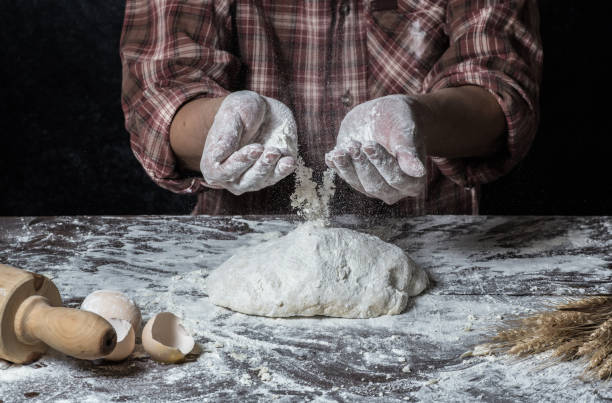 istock Man preparing bread dough on wooden table in a bakery close up 942552446