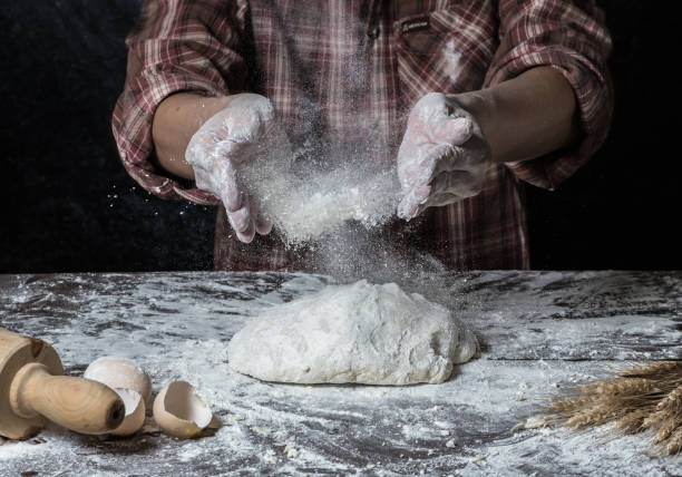 istock Man preparing bread dough on wooden table in a bakery close up 942552464