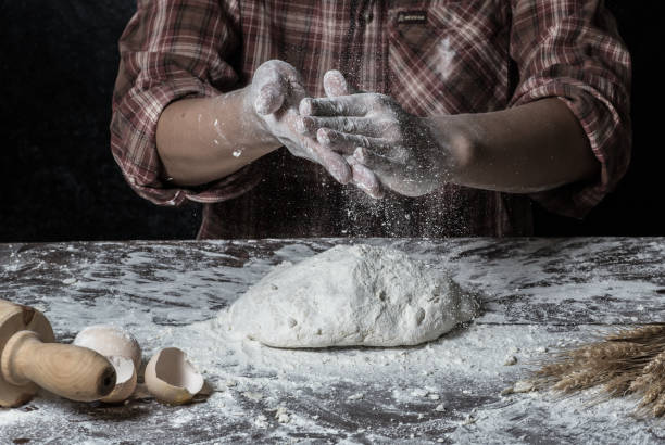 istock Man preparing bread dough on wooden table in a bakery close up 942552916