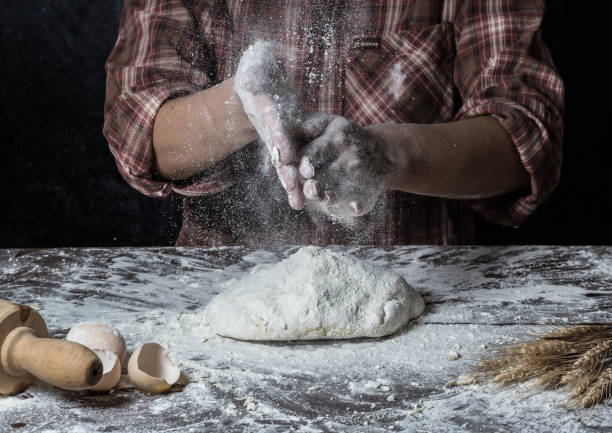 istock Man preparing bread dough on wooden table in a bakery close up 942553048