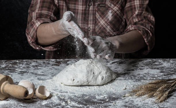 istock Man preparing bread dough on wooden table in a bakery close up 942553054