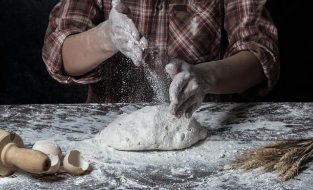 istock Man preparing bread dough on wooden table in a bakery close up 942553058