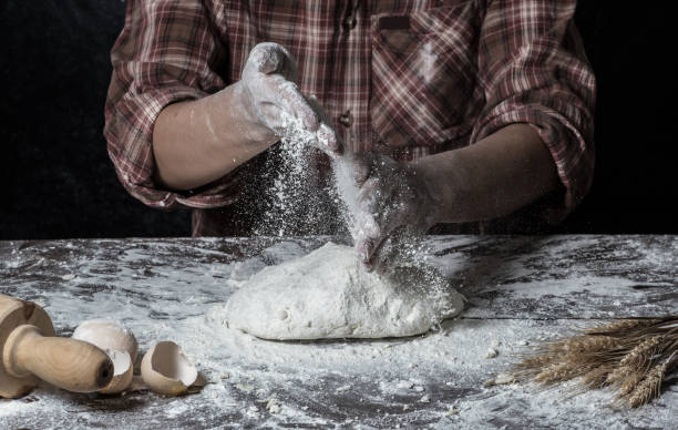 istock Man preparing bread dough on wooden table in a bakery close up 942555364