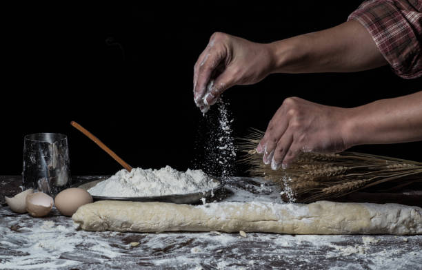 istock Man preparing bread dough on wooden table in a bakery close up 942555376