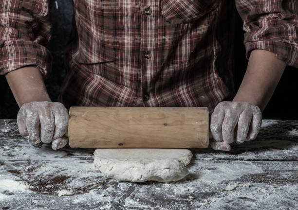 istock Man preparing bread dough on wooden table in a bakery close up 942555378